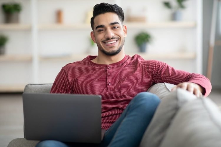 smiling-arab-guy-reclining-on-sofa-with-laptop-W2DPVB2-1.jpg